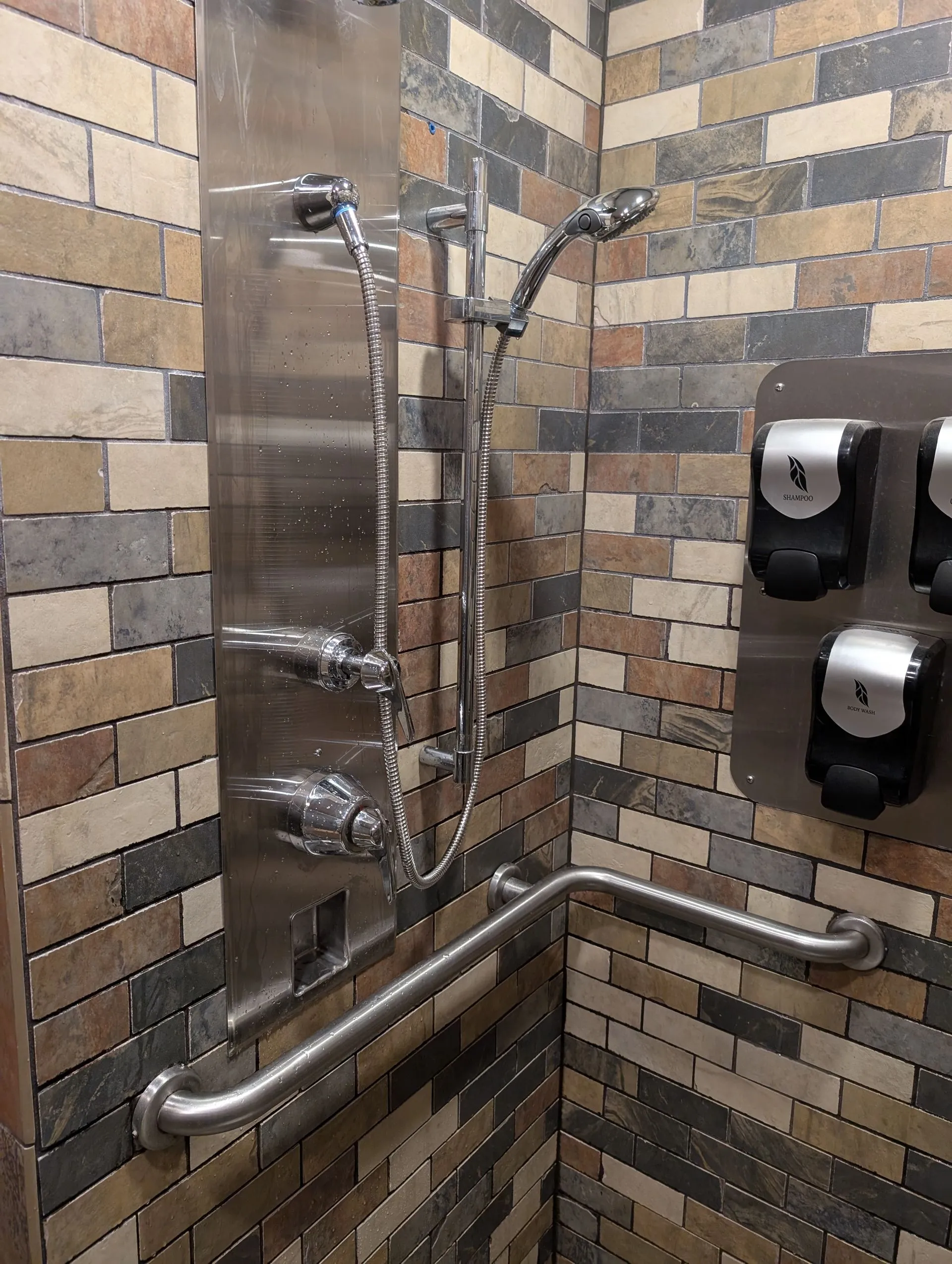 Accessible shower stall with grab bars, handheld showerheads, and wall-mounted dispensers on tiled walls