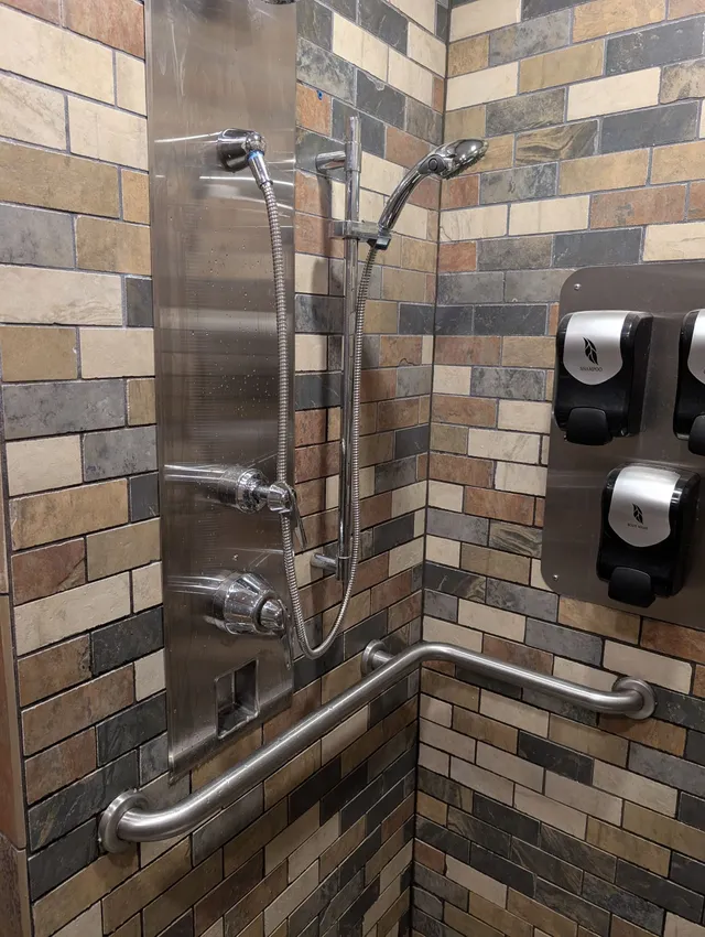 Accessible shower stall with grab bars, handheld showerheads, and wall-mounted dispensers on tiled walls