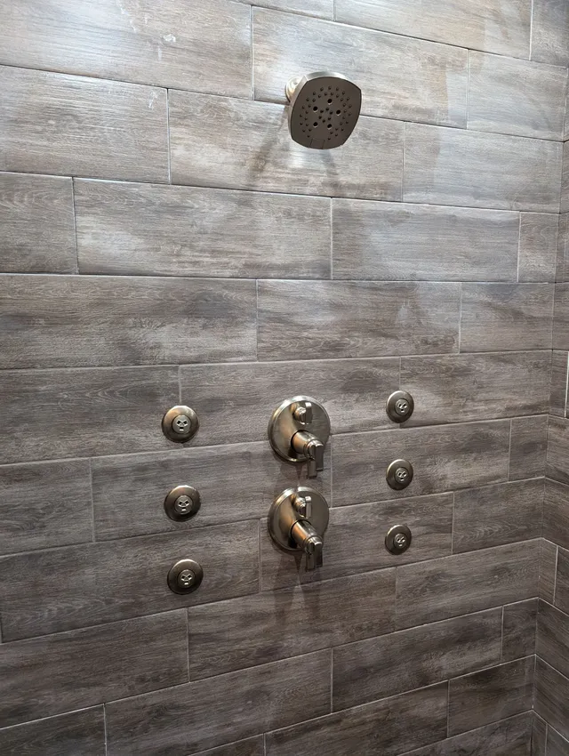 Dark tiled shower wall with metal knobs and a circular showerhead opening