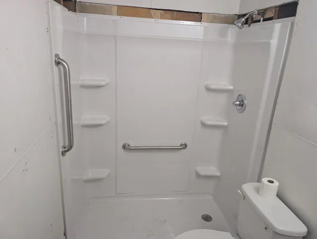 Accessible shower stall with grab bars, fold-down seat, and handheld showerhead
